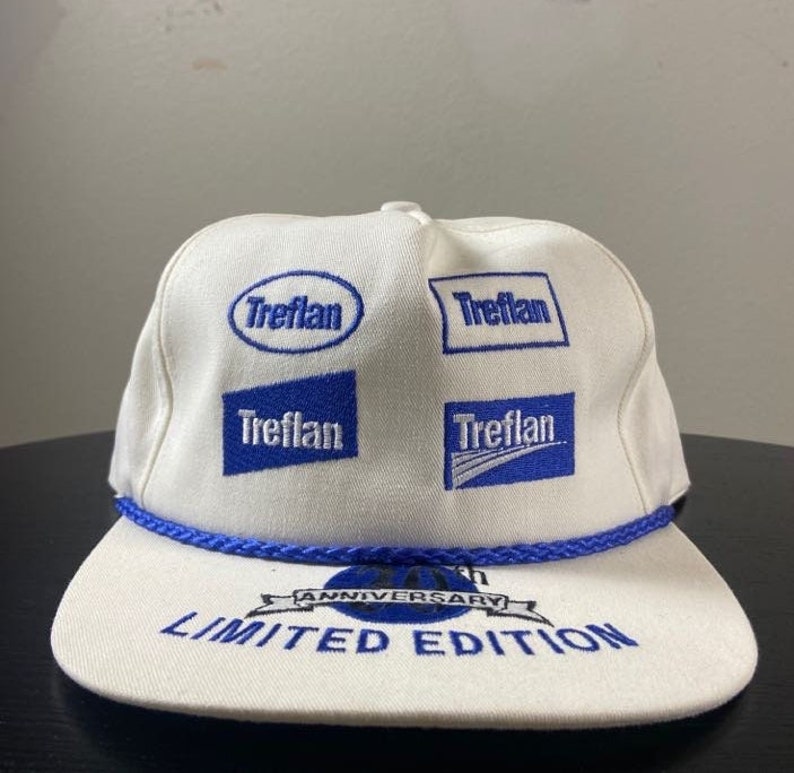 May include: White baseball cap with blue embroidered logos of the brand "Treflan" and the text "Anniversary Limited Edition".