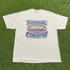 May include: White t-shirt featuring a graphic of the Titanic ship with the text "TITANIC WHITE STAR LINE MAIDEN 1912 VOYAGE CREW" in blue and red. The shirt is made of a soft, comfortable material.