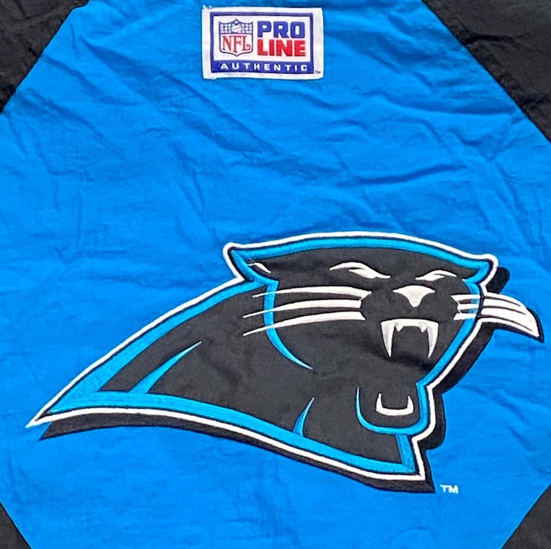 Peut inclure: Veste bleue et noire avec le logo des Panthers de la Caroline. Le logo est une panth&egrave;re noire avec des accents blancs et un contour bleu. La veste porte un &eacute;cusson "Pro Line NFL Authentic".