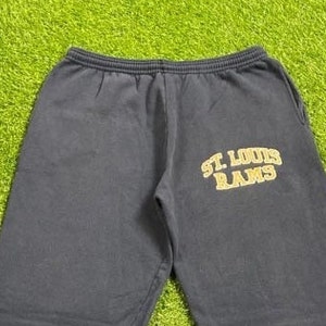 Può includere: Pantaloni della tuta blu navy con la scritta "ST. LOUIS RAMS" in lettere dorate. I pantaloni della tuta hanno un elastico in vita e tasche. Il tessuto sembra essere un materiale morbido e confortevole.
