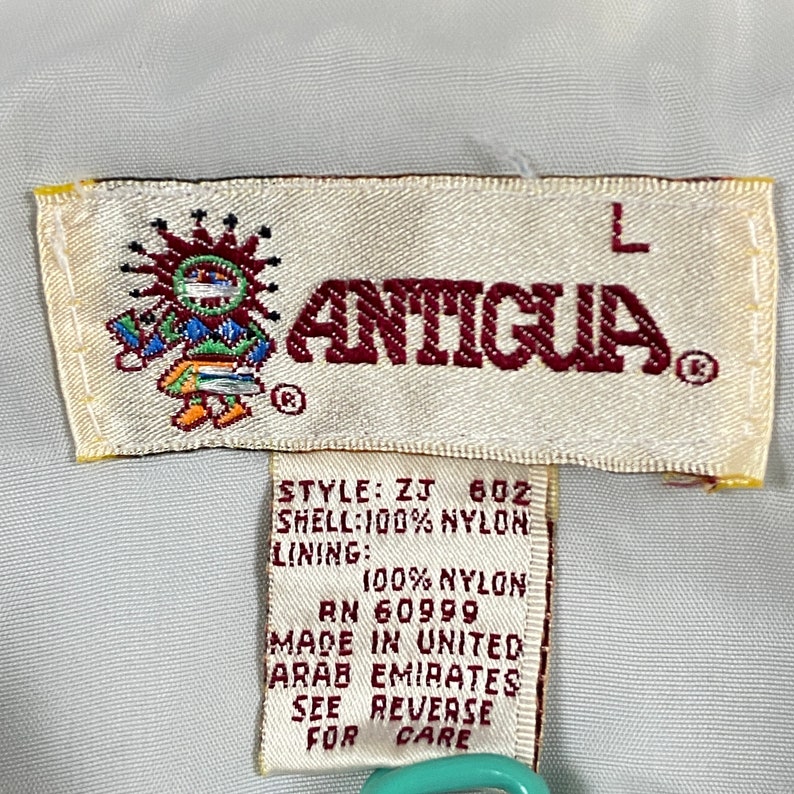 May include: A white tag with brown trim and the word "ANTIGUA" in red letters. The tag also includes the style number "ZJ 602", fabric details, and the words "Made in United Arab Emirates".