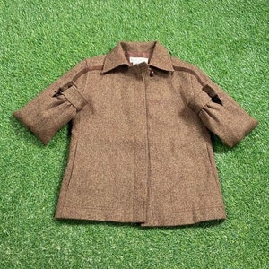 May include: A brown tweed jacket with a brown trim around the sleeves and collar. The jacket has a zipper closure and a brown button.