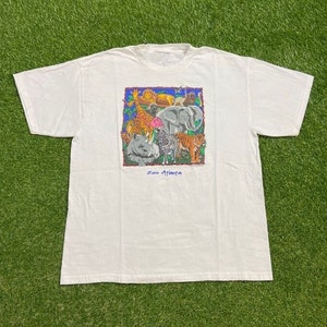 May include: White t-shirt with a colorful graphic of various animals, including a giraffe, elephant, zebra, and tiger. The graphic is surrounded by a blue border and the text "Zoo Atlanta" is printed below it.