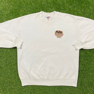 Könnte beinhalten: Weißer Crewneck-Pullover mit einem Aufdruck eines Sonnenuntergangs und dem Text "Dry Land" mit den Wörtern "Entertainment" und "Orlando" darunter.