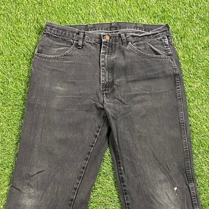 Könnte beinhalten: Eine schwarze Jeans mit geradem Bein. Die Jeans hat ein klassisches Fünf-Taschen-Design und einen Knopfverschluss.