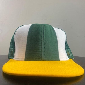 May include: A trucker hat featuring a yellow peak, a white and green front panel, and a green mesh back. The hat has a classic, sporty design.
