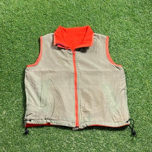 May include: A reversible vest with a beige outer layer and a bright orange inner layer. The vest has a zipper closure and two pockets on the front.
