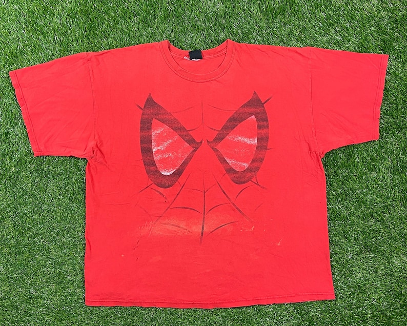 Puede incluir: Camiseta roja con un estampado gr&aacute;fico de la cara de Spider-Man. El dise&ntilde;o es en negro y rojo y presenta los ojos y la telara&ntilde;a de Spider-Man.