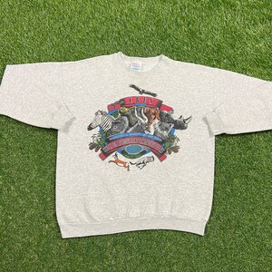 May include: Gray sweatshirt with a graphic of a group of animals, including a zebra, rhino, and a lion. The graphic is surrounded by a red and blue banner with the text "CRIS" and "ENDANGERED SPECIES" in white.