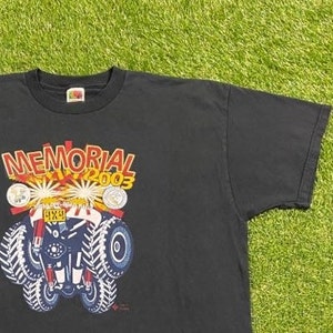 Może przedstawiać: Czarny T-shirt z grafiką przedstawiającą czerwony, biały i niebieski samoch&oacute;d 4x4 z napisem "MEMORIAL DAY 2003" nad nim.