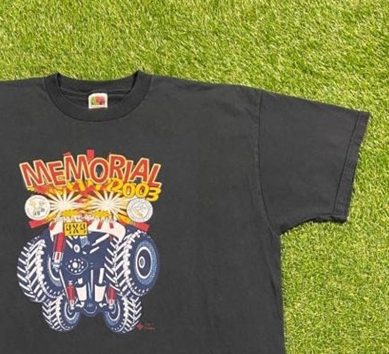 Może przedstawiać: Czarny T-shirt z grafiką przedstawiającą czerwony, biały i niebieski samoch&oacute;d 4x4 z napisem "MEMORIAL DAY 2003" nad nim.