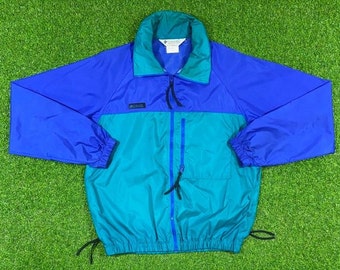 Könnte beinhalten: Eine blaue und türkisfarbene Nylonjacke mit Reißverschluss und Kordelzug an der Taille. Die Jacke hat ein Columbia-Logo auf der linken Brust.
