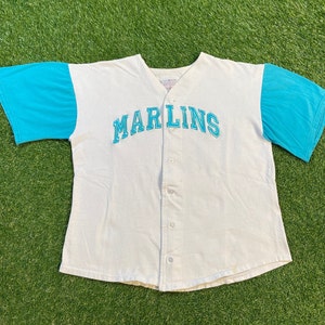 May include: White baseball jersey with blue sleeves and the word "Marlins" in blue lettering across the chest.