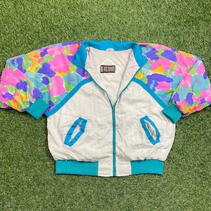 May include: A white windbreaker jacket with a blue zipper and turquoise trim. The sleeves have a colorful floral print with pink, purple, yellow, and blue flowers.