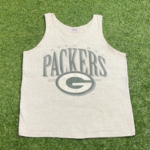 Puede incluir: Camiseta sin mangas gris claro con las palabras "GREEN BAY PACKERS" en letras verdes. Debajo del texto hay un óvalo verde con una "G" verde en su interior. La camiseta sin mangas es sin mangas.