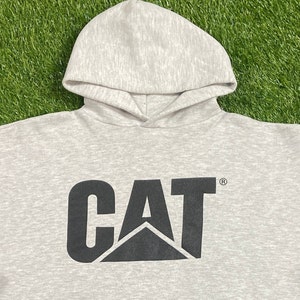 May include: A gray hooded sweatshirt with a black CAT logo printed on the front. The logo features a black triangle with the letters CAT in a bold black font.