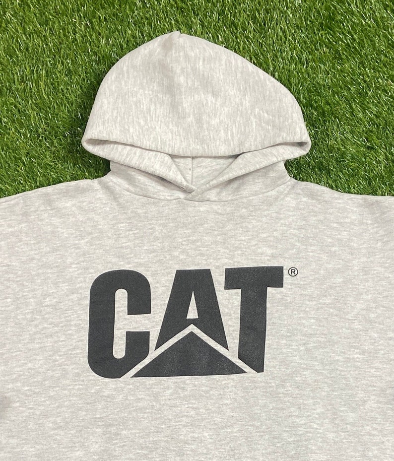 May include: A gray hooded sweatshirt with a black CAT logo printed on the front. The logo features a black triangle with the letters CAT in a bold black font.