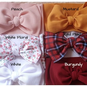 May include: Six different colors of fabric headbands with bows. The colors are peach, mustard, white floral, red plaid, white, and burgundy.