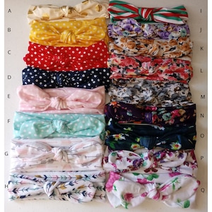May include: A set of 15 colorful headbands with different patterns, including polka dots, floral prints, and arrows. The headbands are made of soft fabric and have a knotted bow design.