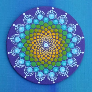 May include: A circular mandala artwork in purple, featuring a dot pattern. The centre is yellow, fading to green and blue, with white details. The background is a gradient of blue shades.