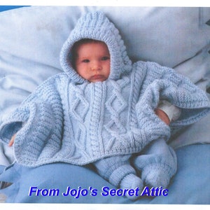 Peut inclure: Un poncho bébé en tricot bleu clair avec une capuche et un motif en câble. Le poncho est porté par un bébé allongé sur une couverture bleue.