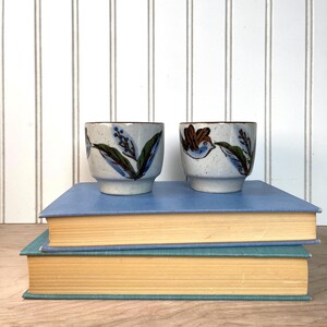 May include: A set of three ceramic mugs with a speckled, matte finish. The mugs are in shades of cream, light gray, and dark gray. Each mug has a simple, minimalist design, perfect for coffee or tea.