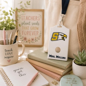 May include: A white rectangular plastic ID badge holder featuring a yellow and black eagle mascot logo with the letter S and the text MRS. MULLINS in navy blue. The holder is attached to a dark navy blue lanyard with a silver metal swivel hook.