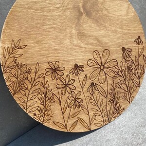 Peut inclure: Un plateau de service rond en bois avec un motif de fleurs et de feuilles grav&eacute; au laser autour du bord. Le plateau est en bois brun clair et a une finition naturelle.