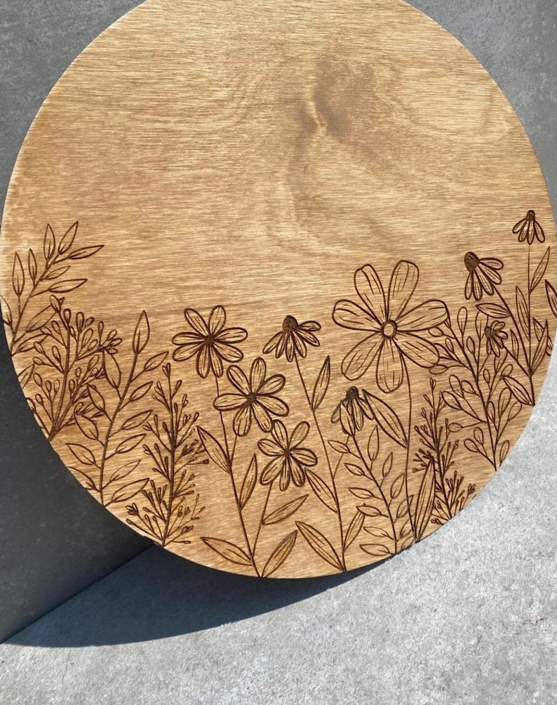 Peut inclure: Un plateau de service rond en bois avec un motif de fleurs et de feuilles grav&eacute; au laser autour du bord. Le plateau est en bois brun clair et a une finition naturelle.