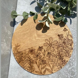 Peut inclure: Un plateau de service rond en bois avec un motif floral grav&eacute; &agrave; la surface. Le motif pr&eacute;sente une vari&eacute;t&eacute; de fleurs et de feuilles de couleur brun fonc&eacute;.