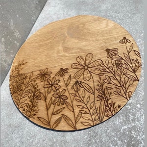 Peut inclure: Un dessous de verre rond en bois avec un motif de fleurs et de feuilles grav&eacute; au laser. Le dessous de verre est brun clair et le motif est brun fonc&eacute;.