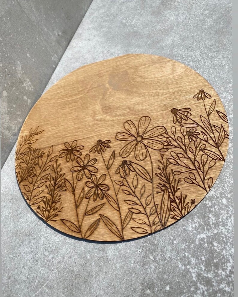 Peut inclure: Un dessous de verre rond en bois avec un motif de fleurs et de feuilles grav&eacute; au laser. Le dessous de verre est brun clair et le motif est brun fonc&eacute;.