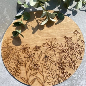 Peut inclure: Un plateau de service rond en bois avec un motif de fleurs et de feuilles grav&eacute; au laser. Le plateau est brun clair et pr&eacute;sente un grain de bois naturel.