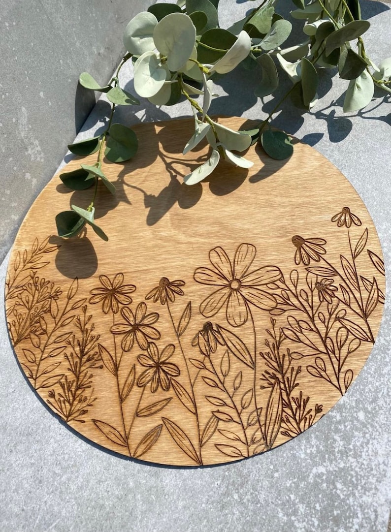 Peut inclure: Un plateau de service rond en bois avec un motif de fleurs et de feuilles grav&eacute; au laser. Le plateau est brun clair et pr&eacute;sente un grain de bois naturel.