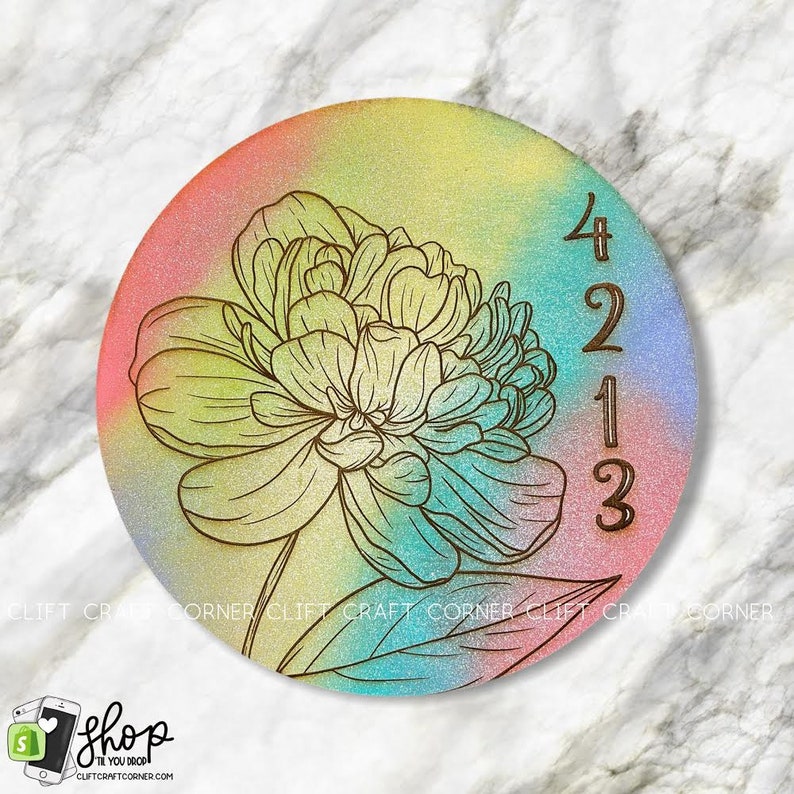 K&ouml;nnte beinhalten: Ein runder Untersetzer aus Holz mit einem farbenfrohen Ombre-Design in den Farben Rosa, Gelb, Blau und Gr&uuml;n. Ein Blumenmuster ist in den Untersetzer ge&auml;tzt, ebenso die Zahlen 4213.