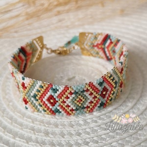 May include: A beaded bracelet with a geometric pattern in shades of red, green, gold, and white. The bracelet has a gold clasp.