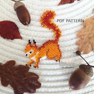 Może przedstawiać: Koralik wiewiórka w odcieniach pomarańczy, czerwieni i bieli, z czarnymi akcentami, jest głównym punktem. Obraz zawiera żołędzie i jesienne liście. Tekst na obrazie brzmi "PDF PATTERN" i "Liliaazalee".
