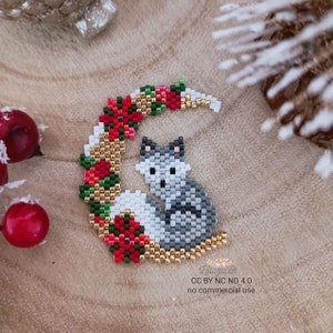 Könnte beinhalten: Ein Fuchs aus Perlen, der auf einem goldenen Halbmond aus Perlen sitzt. Der Mond ist mit roten und grünen Weihnachtssternen verziert.