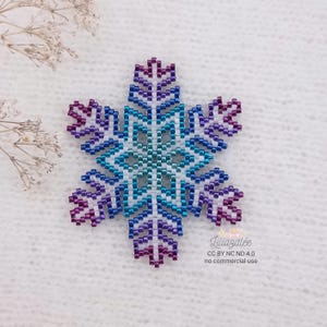 Peut inclure: Une décoration de flocon de neige en perles avec un dégradé de couleurs violet, bleu et blanc. Le flocon de neige est fait de petites perles rondes et a un design symétrique.