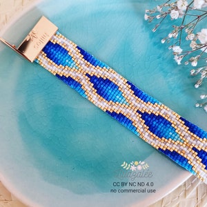 Peut inclure: Un bracelet en perles bleu, blanc et or avec un motif géométrique. Le bracelet a un fermoir en or.