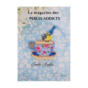 May include: A blue and white teacup with a floral pattern and a gold rim, with a small blue and yellow bird perched on the rim. The teacup is on a white background with a floral pattern. The text "Le magazine des PERLES ADDICTS" is at the top of the image. The text "Jardin Anglais" is below the teacup. The text "Numéro 12 MAI 2023" is in the lower left corner. The text "Liliazalée Le Bazar de Milipuce" is in the lower right corner.
