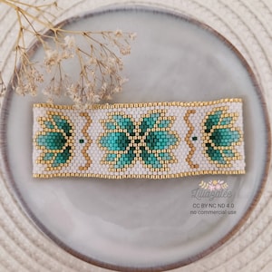 Peut inclure: Un bracelet de perles avec un fond blanc et un motif floral en turquoise et or. Le bracelet présente un motif répété de fleurs turquoise et d'accents dorés. Le bracelet mesure environ 3,8 cm de large.