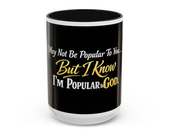 Op de afbeelding: Een witte keramische mok met een zwarte buitenkant en een witte binnenkant. De mok heeft de tekst "I May Not Be Popular To You... But I Know I'm Popular To God" in witte en gouden letters.