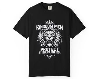 Op de afbeelding: Zwart t-shirt met een witte afbeelding van een leeuwenkop, een kroon en de tekst "KINGDOM MEN PROTECT THEIR FAMILIES". Het ontwerp is gecentreerd op de voorkant van het shirt.