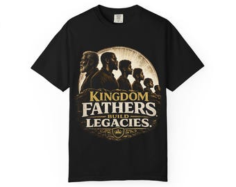 Op de afbeelding: Zwart T-shirt met de tekst "KINGDOM FATHERS BUILD LEGACIES" in goud en bruin. De afbeelding toont silhouetten van mannen en jongens voor een zon. Het shirt heeft een ronde hals en korte mouwen.