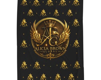 Op de afbeelding: Zwarte deken met een gouden embleem met de tekst "ALICIA BROWN GLOBAL". Het embleem bevat een kroon, vleugels en de letters "ABG". De deken heeft een herhalend patroon van gouden kronen en de letters "A&G".