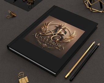 Op de afbeelding: Zwart notitieboek met het gouden logo "Alicia Brown Global" op de kaft. Het logo toont een kroon, vleugels en de letters "ABG". Gouden paperclips en potloden zijn rond het notitieboek geplaatst op een donkergrijze ondergrond.