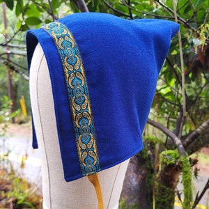 May include: A blue hooded hat with a gold and teal patterned trim. The hat is displayed on a white mannequin head.