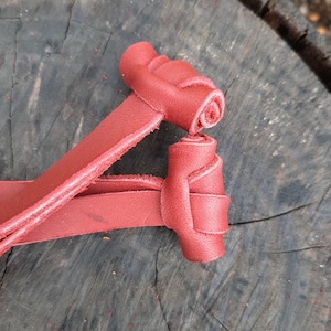 May include: Two red leather rose-shaped embellishments. The leather is a deep red color, and the roses are intricately crafted. The background is a weathered, dark wood surface.