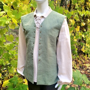 May include: A sage green sleeveless vest featuring a front opening with a series of small metal eyelets, worn over a light beige long-sleeved shirt with a lace-up collar detail. The vest has a straight hem and a simple, unadorned construction.